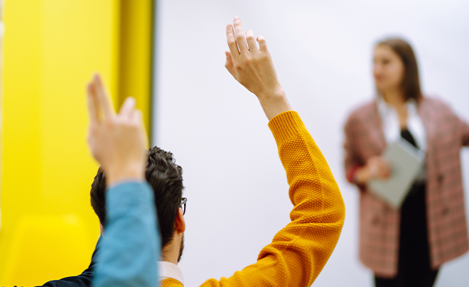 grupo de estudiantes en un aula levanta la mano con entusiasmo para responder a una pregunta del docente